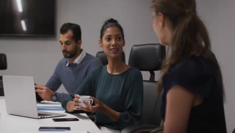 Two-diverse-female-office-colleagues-talking-to-each-other-in-meeting-room-at-office