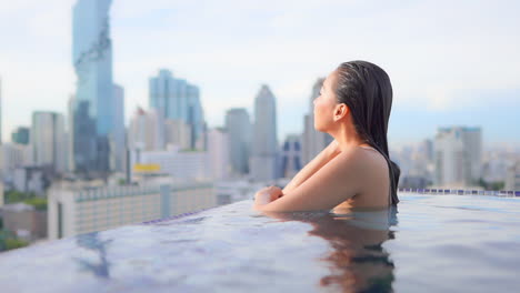 a young woman inside rooftop infinity pool on amazing blurred bangkok cityscape background enjoying sunset