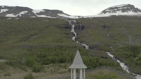 Church-tower-with-cross-on-top-and-stunning-mountains-in-background,-aerial