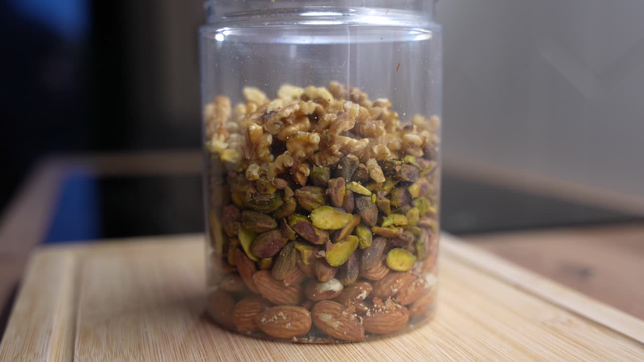 Close-up of mixed nuts filling plastic jar. Prep for clean healthy diet snacks