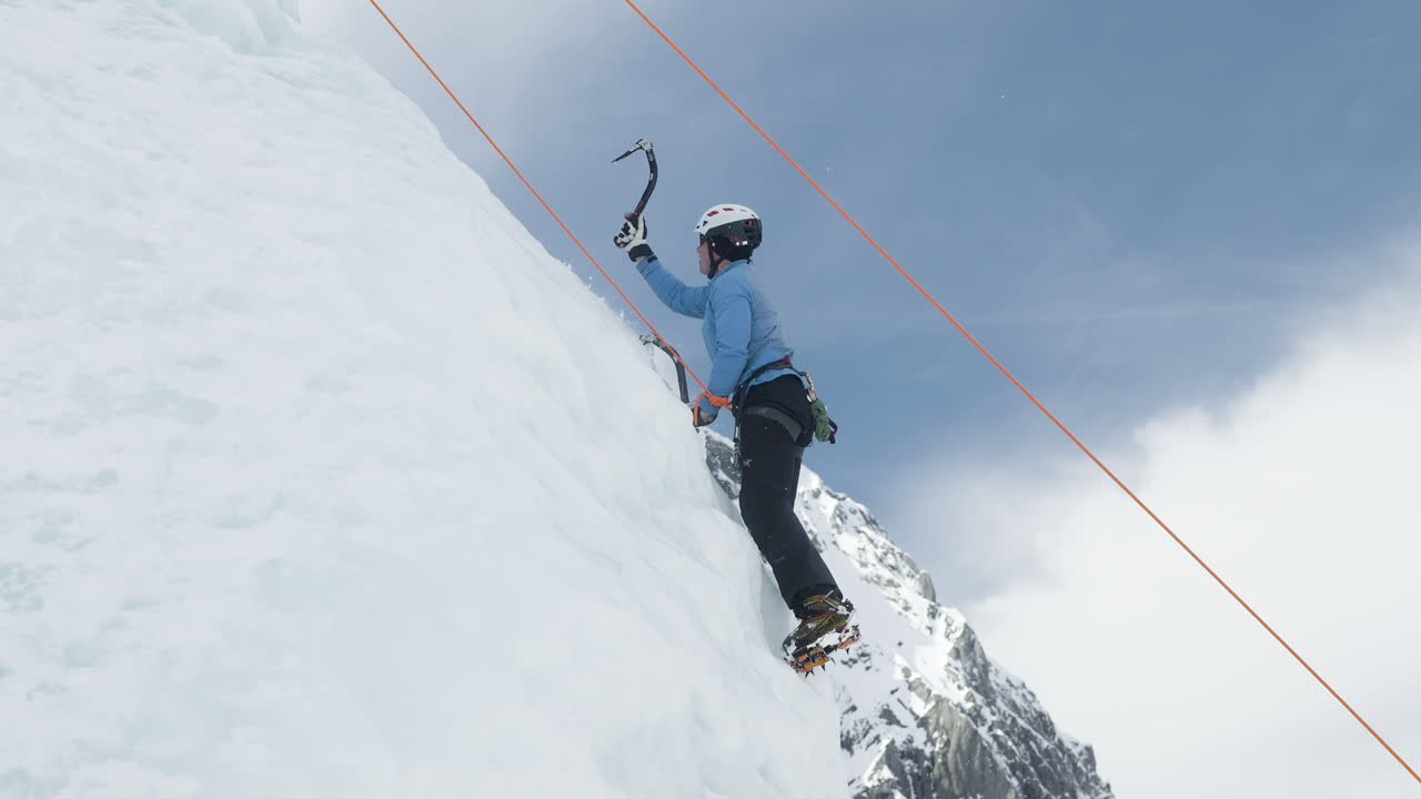 Profesjonell mannlig isklatrer bruker utstyr for å bestige en isete fjellside, sett fra siden