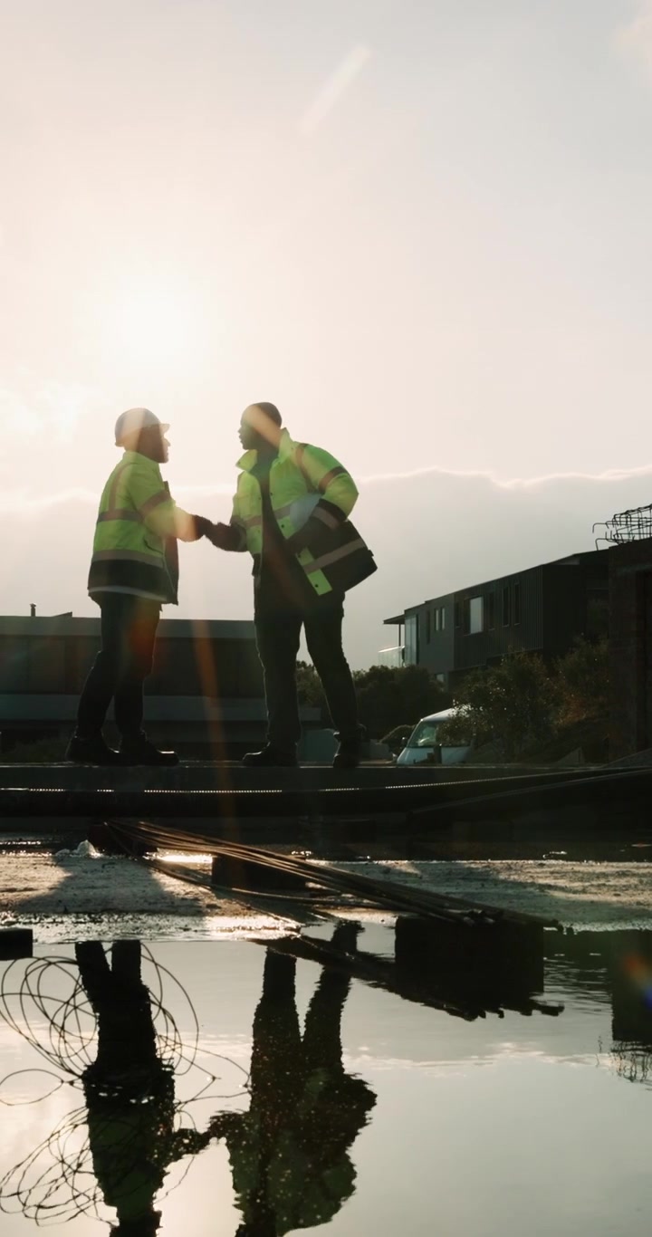 Construction Workers Shaking Hands at Building Site at Sunset
