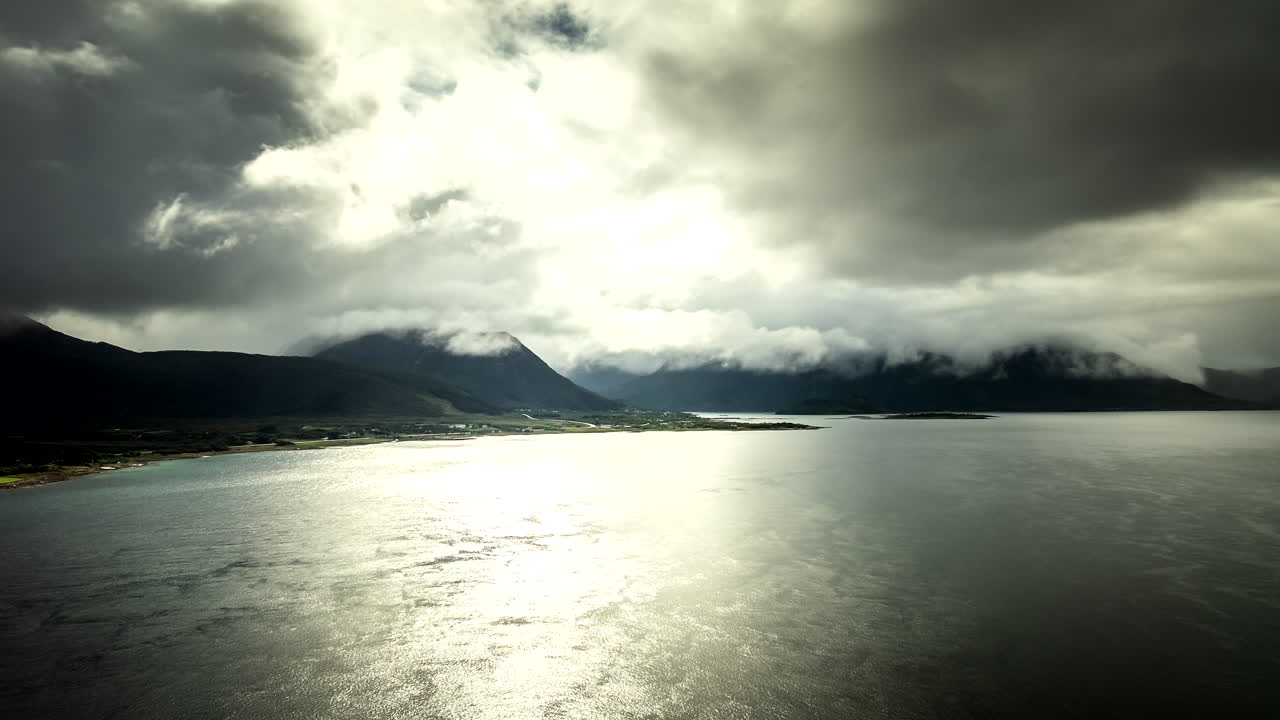 Cinematic drone hyperlapse over shimmering sea and moody clouds near Sortland, Vesterålen, Northern Norway, with dramatic light breaking across water and distant mountains