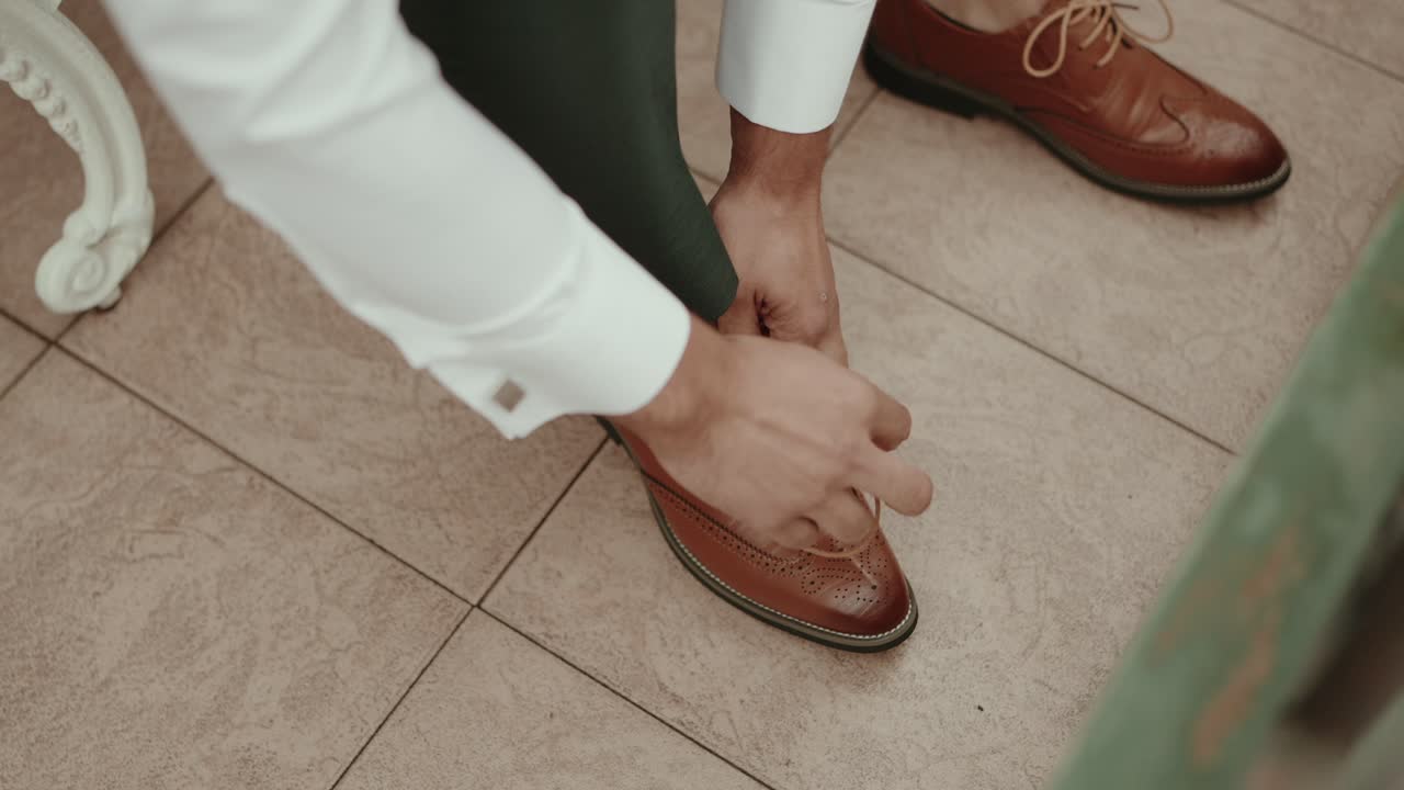 Close up of a man tying laces on elegant brown leather shoes on tiled floor