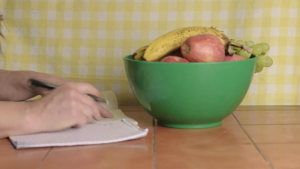 Woman studying at kitchen table with bowl of fruit