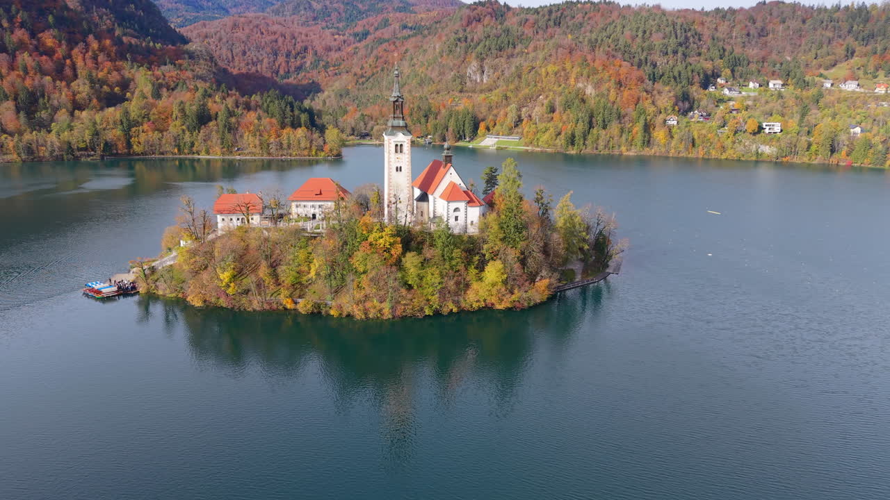 Filmato aereo maestoso che orbita attorno all'iconica chiesa sull'isola del Lago di Bled, circondata da una foresta autunnale