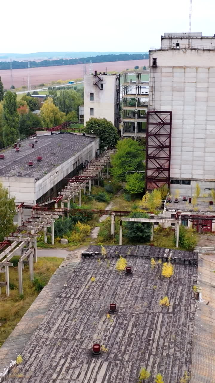 Abandoned factory with many ruined buildings. Old brick thick pipe on empty plant. Deserted industrial territory. Aerial view.. Vertical video