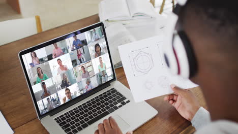 estudiante universitario afroamericano que sostiene notas mientras tiene una videoconferencia en una computadora portátil en casa