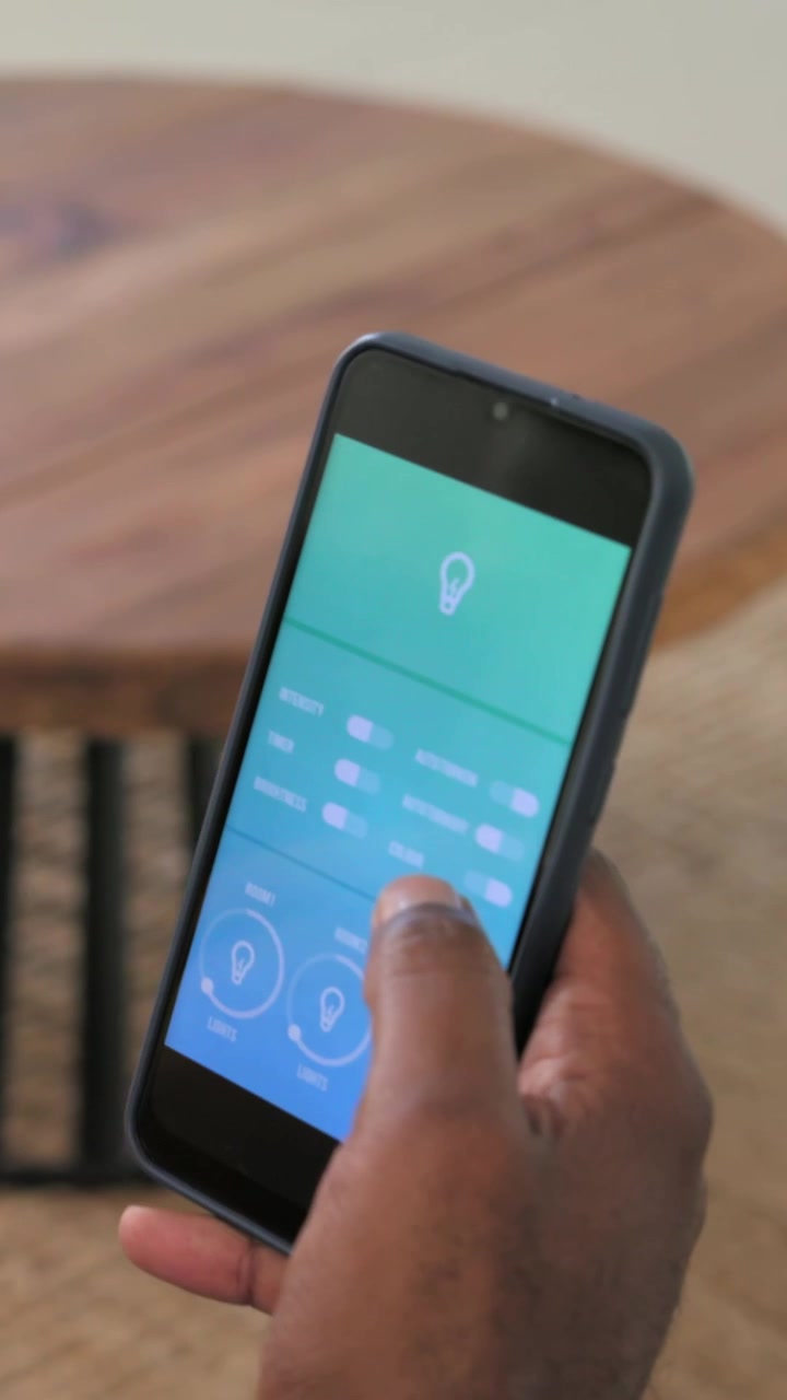 Vertical video: Tapping phone with right hand wearing band, sliding dials on couch adjusting lights