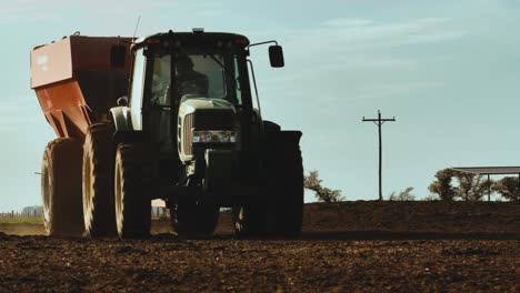 Tractor-driving-on-farm-land,-passing-by-camera