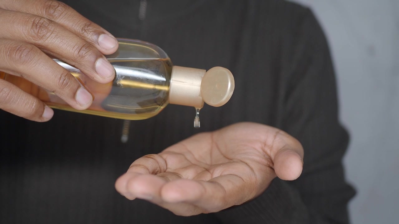 Pessoa Derramando Óleo Dourado de uma Garrafa na Palma da Mão