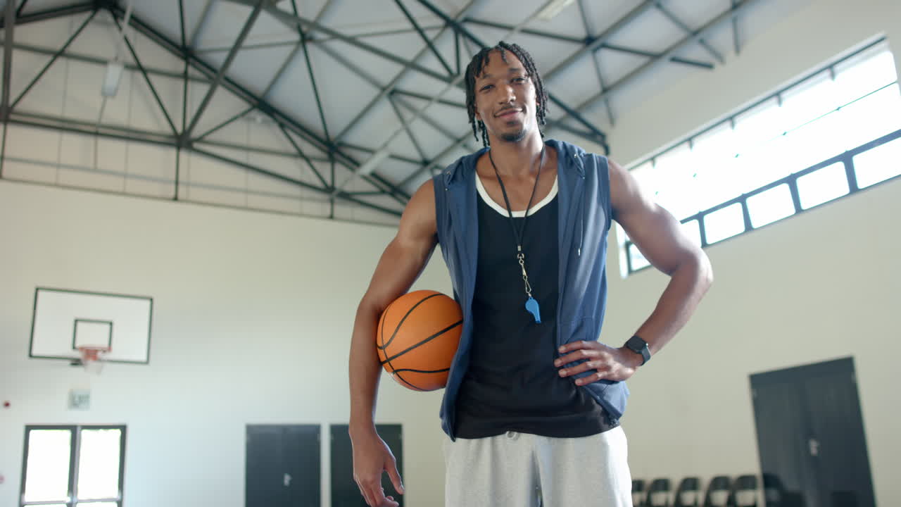 Holding basketball, coach standing confidently in gymnasium, ready for practice