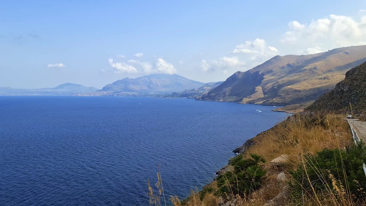 Stunning panoramic panning view of Sicilian Riserva dello Zingaro natural reserve in Sicily with yellow car on coastal road