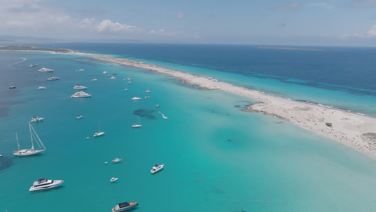 Aerial shot of leisure boats anchored near the white sandy shore of Ses Illetes, with calm turquoise waters and a serene Mediterranean backdrop