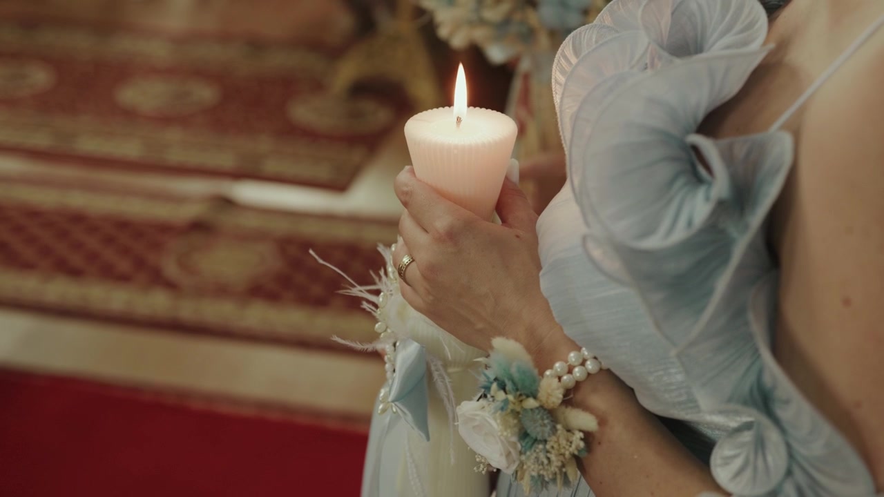 Close-up of a bride holding a lit candle during a traditional wedding ceremony inside a church.