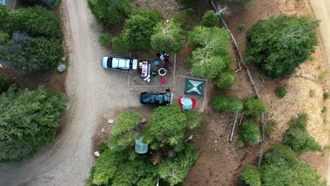 Vista-Superior-Aérea-A-Vista-De-Pájaro-De-Un-Pequeño-Campamento-Con-Tiendas-De-Campaña,-Automóviles,-Un-Pozo-De-Fuego-Y-Grandes-Pinos-Verdes-Que-Los-Rodean-En-Una-Cálida-Y-Soleada-Mañana-De-Verano-En-El-Embalse-De-Anderson-Prado-En-Beaver,-Utah