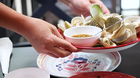 hands serving boiled ark clams with dipping sauce in phuket, thailand