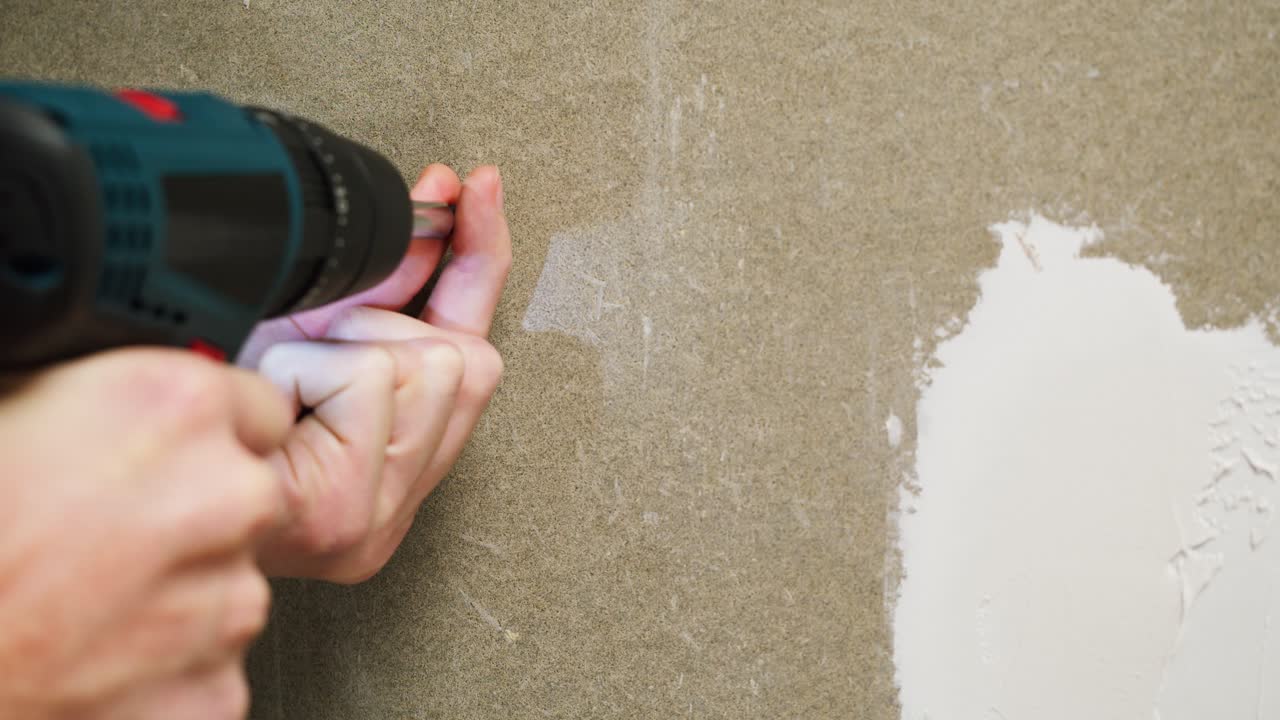 Manos usando un taladro eléctrico para atornillar en una pared