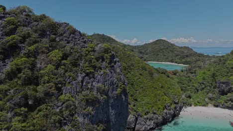 drone ascends and zooms into a secluded turquoise lagoon framed by lush hills under bright midday skies in april on phi phi islands, thailand.