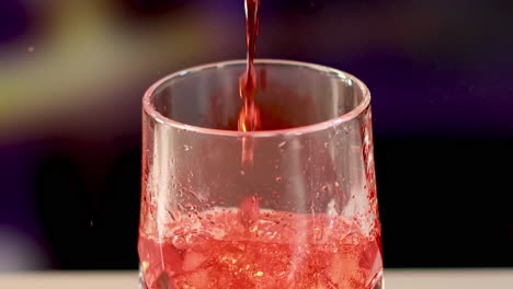 a sequence of red liquid being poured over ice in a glass, set against a blurred background.