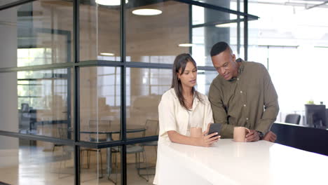 discussing work, colleagues looking at smartphone and holding coffee mugs in office