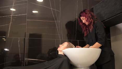 beauty and people concept – happy young woman with hairdresser washing her hair in hairdressing salon. working day inside the hair salon, hairdresser washing hair.