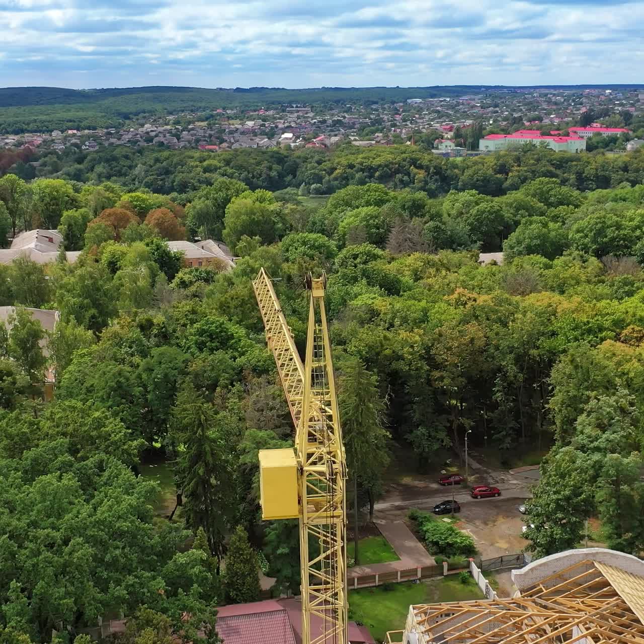High crane works on building site with a house. Construction of a modern ecologic skyscraper with many green trees nearby