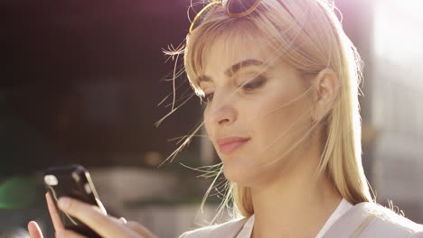 Beautiful-blonde-woman-using-smartphone-solar-flare-sunlight-energy-concept