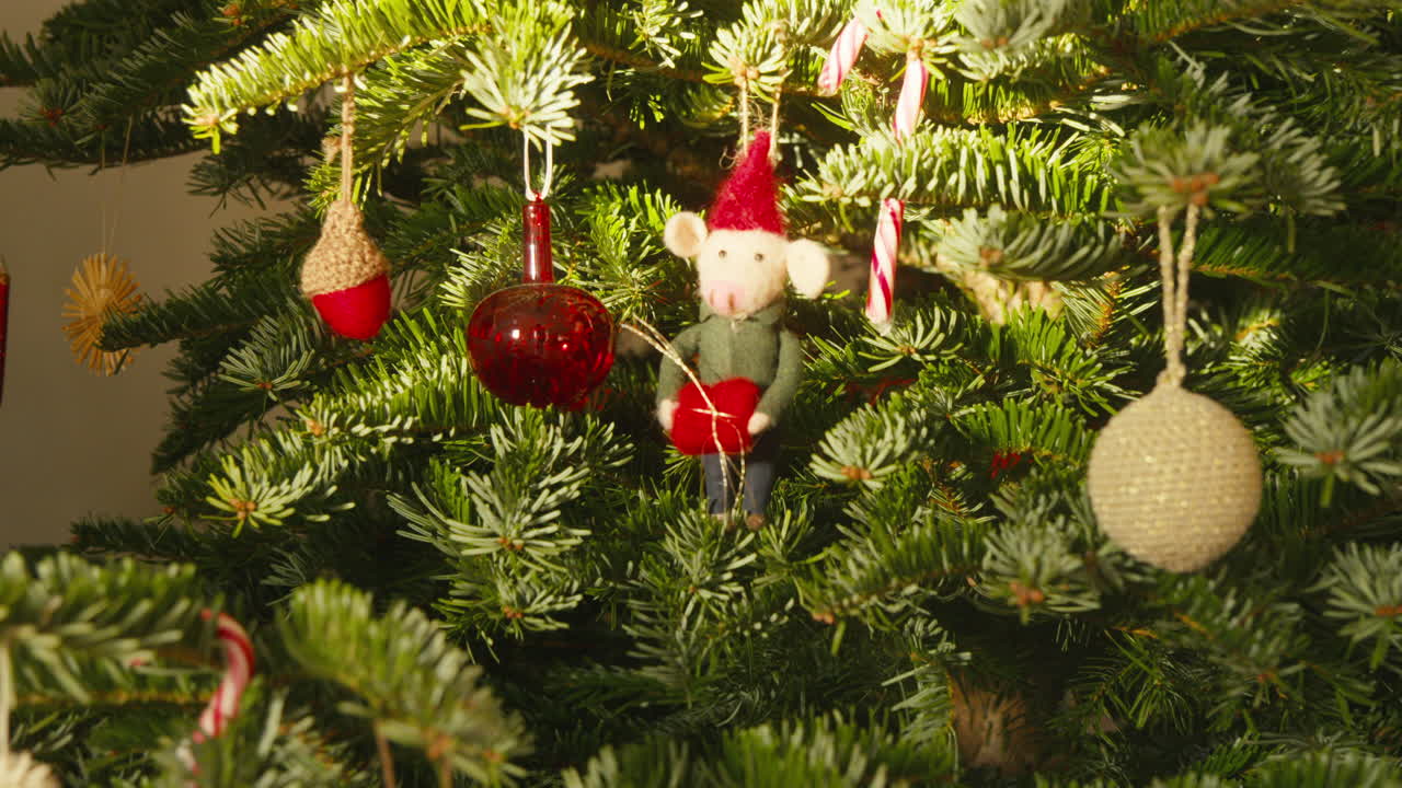 Árvore de Natal decorada em estilo escandinavo com enfeites coloridos e figura de rato festivo durante o dia.