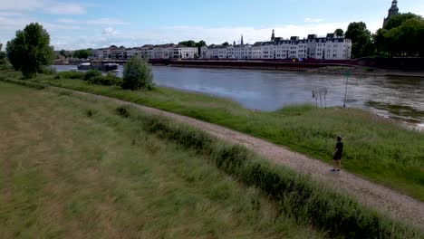 vista aérea de un corredor de trail masculino haciendo ejercicios de respiración y concentrándose antes de despegar para su carrera mientras un barco de carga pasa por el río ijssel