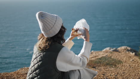 travel girl eating sandwich at rocky cliff edge. vertically tourist take break