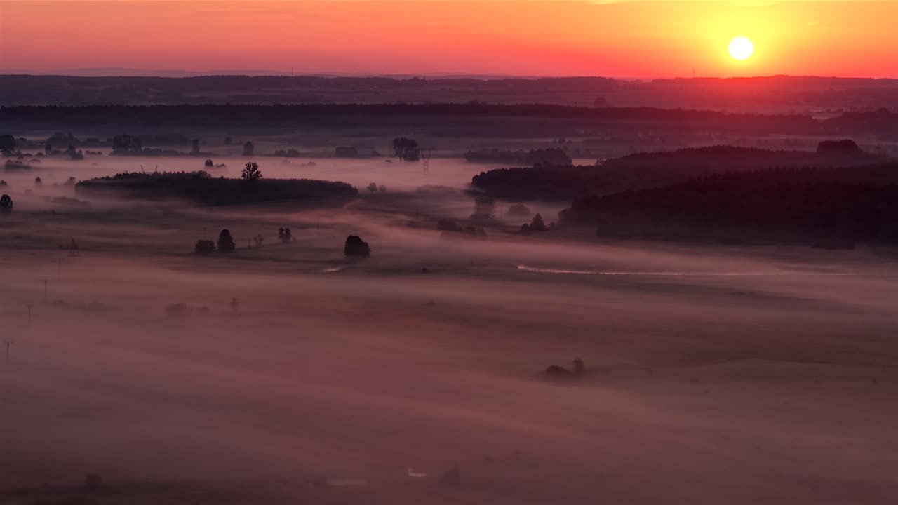 Aerial of foggy fields and sunrise over Poland's Nida valley, serene nature view