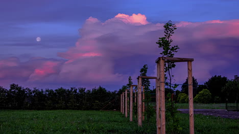 Toma-De-Tiempo-De-Una-Nube-Blanca-Moviéndose-Sobre-Pastizales-Verdes-Con-Luna-Llena-Saliendo-En-El-Fondo-Durante-La-Noche