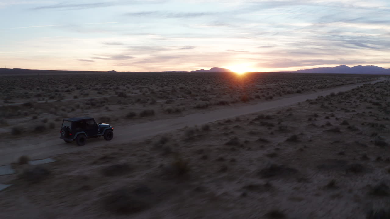 jeep bajando por un sendero de tierra en el desierto de mojave al atardecer - seguimiento aéreo