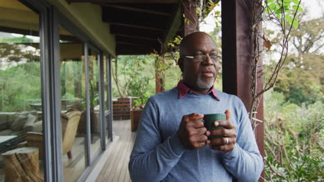 African-american-senior-man-standing-on-balcony-drinking-coffee-and-enjoying-view