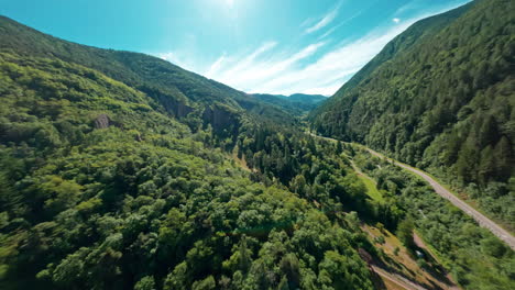 Lush-green-mountains-and-valleys-with-a-winding-road-on-a-sunny-day,-aerial-view