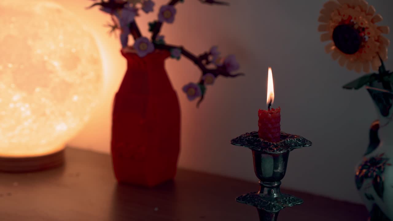 Candela rossa accesa in un portacandele vintage, che crea un'atmosfera accogliente e calda con la sua fiamma tremolante in una stanza buia e romantica.