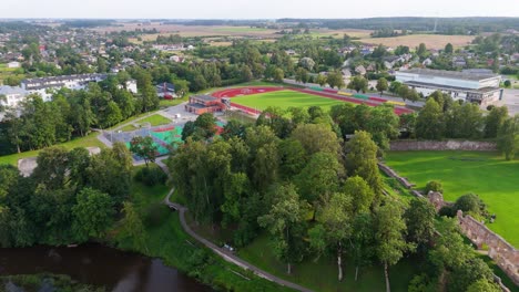 drone sunset view over dobele city aerial timelapse of school, stadium and historic castle ruins in warm evening light, capturing the peaceful atmosphere of latvian urban and cultural landscape