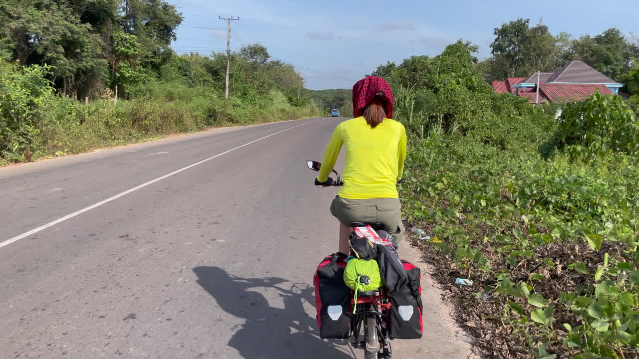 Rear view of women cycling in the street of Laos with trees in the both side of the street 