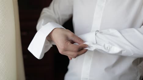 man buttoning his cufflinks on a white dress shirt