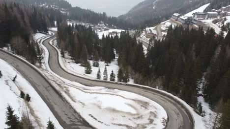 Coche-Rojo-Conduciendo-Por-Serpentinas-Y-Torcidas-Carreteras-Nevadas-En-Las-Montañas-Y-En-Un-Complejo-Hotelero-De-Esquí