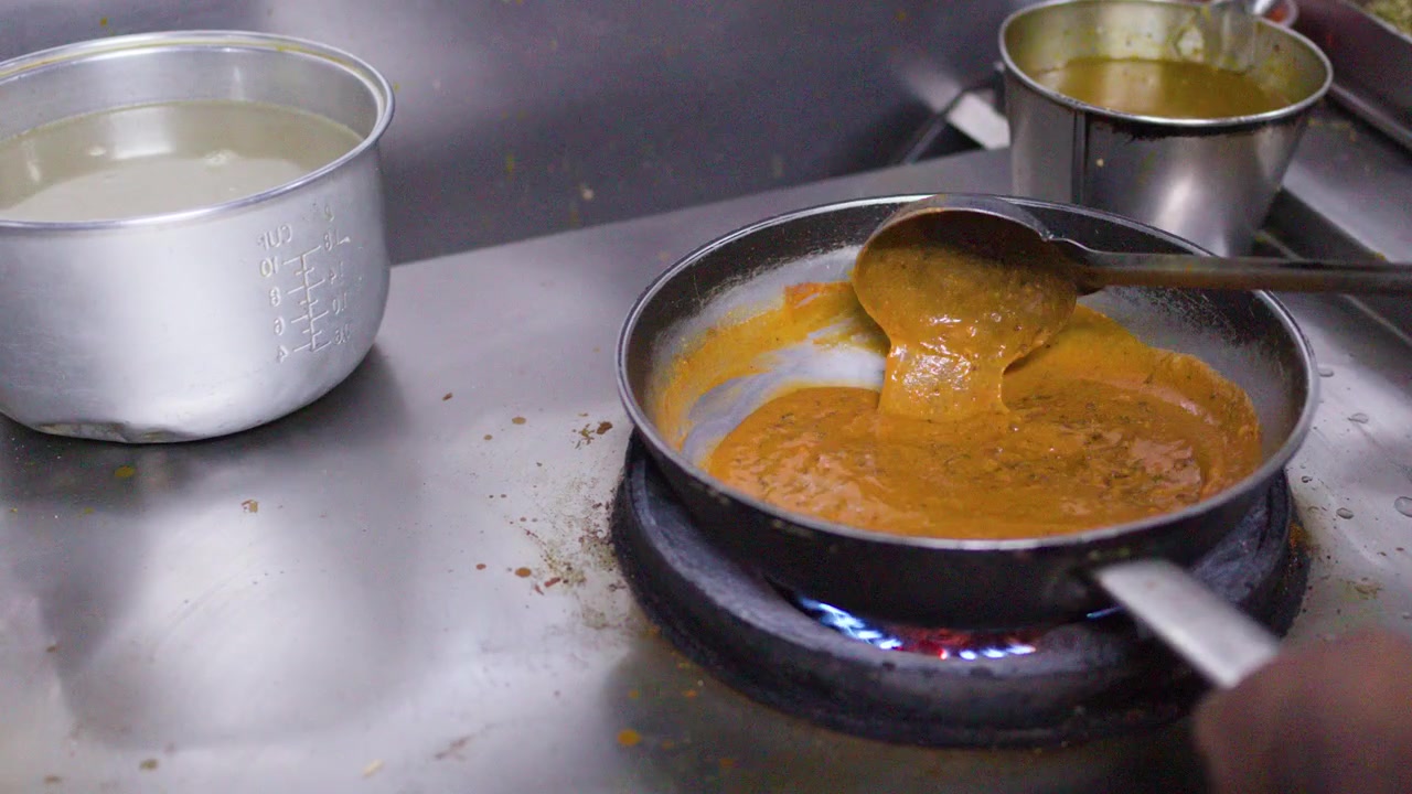 Chef che mescola salsa curry piccante in una cucina di ristorante.