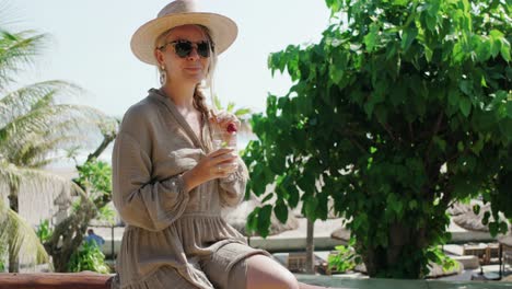 Young-woman-with-sunglasses-and-smoothie-sitting-on-balcony