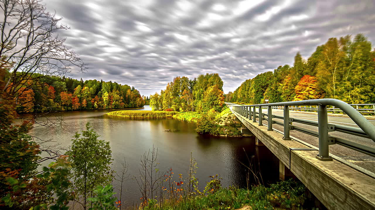 nubes moviéndose en el cielo sobre el paisaje rural y otoñal con un puente que cruza el río o el lago