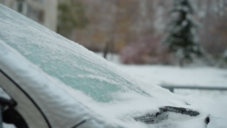 primer plano del parabrisas de un automóvil cubierto de nieve con fondo borroso con árboles congelados y un paisaje nevado, destacando las condiciones heladas del invierno y los detalles atmosféricos