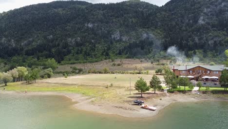 casa de madera al borde de un lago rodeada de un bosque de pinos y montañas