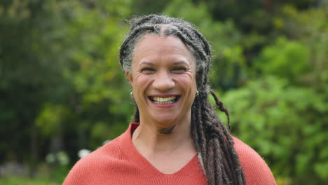 smiling senior woman with dreadlocks enjoying nature in lush green garden