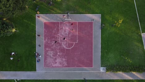 aerial top down circling view directly above pink public basketball court with players surrounded by green area, buenos aires in argentina