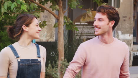 happy young hipster couple walking in city street holding hands and looking at each other, close up