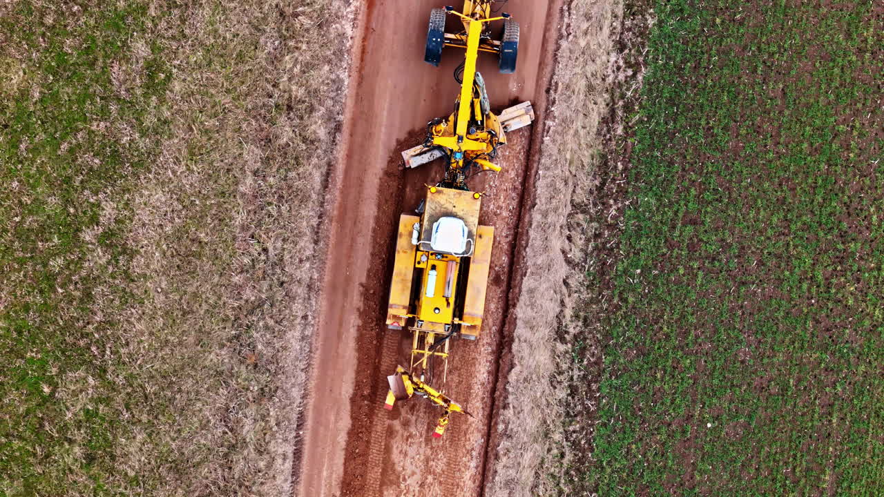 Top down of a yellow tractor driving plowing on narrow road through green fields